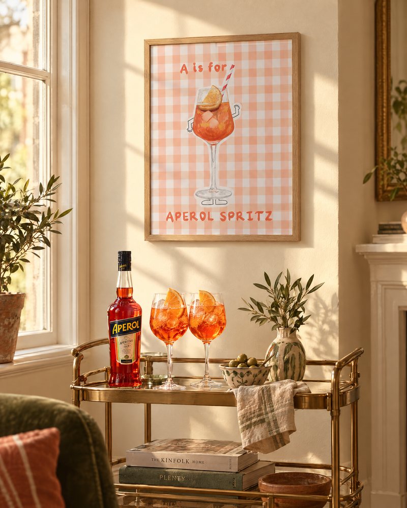 Framed A is for Aperol Spritz print above a brass drinks trolley with two spritz glasses